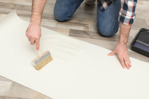 istock Man applying glue onto wall paper on floor, closeup 1314747843