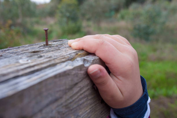 Child boy hand grabbing a board with rusty nail near. Selective focus