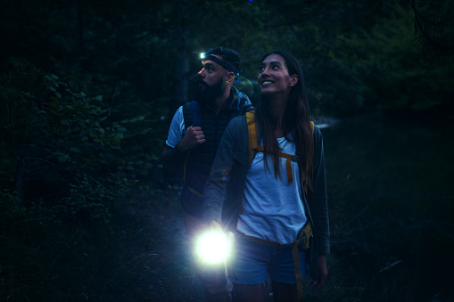 Close up photo of two hikers walking with flashlight at night in the woods.