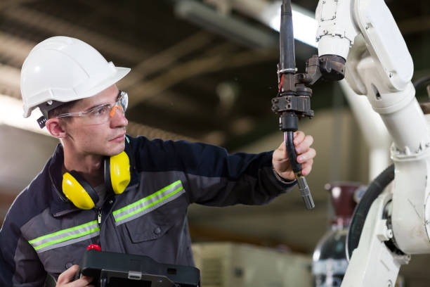 istock Male engineer worker maintenance automatic robotic machine in the factory. Male technician worker working with control automatic robot arm system welding with safety uniform, glasses and helmet 1314755888