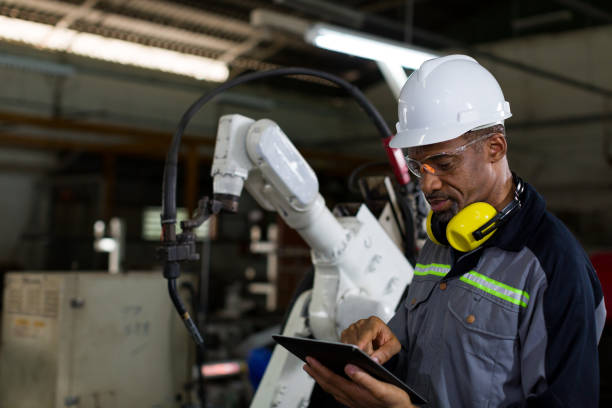 istock African American male engineer worker using tablet with the automatic robotic machine in the factory. Black male technician worker working with control automatic robot arm system welding 1314755890