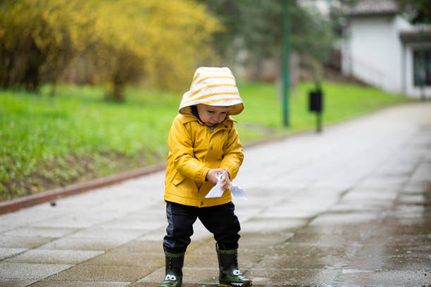 kind spielt mit papierbooten in wasserpfütze - puddle rain boot water stock-fotos und bilder