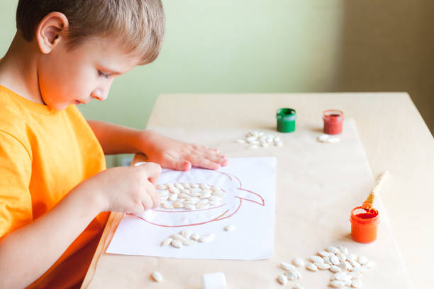 menino feliz fazendo abóbora de sementes em papel branco, conceito de halloween diy - child autumn craft preschooler - fotografias e filmes do acervo