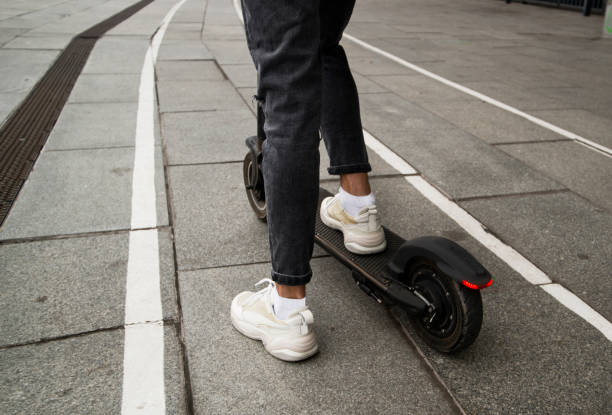 istock Legs of anonymous guy riding modern electric scooter on asphalt path on blurred background of city street. Fast travel concept. Stylish young man rented an e-scooter. White sneakers. 1314759740