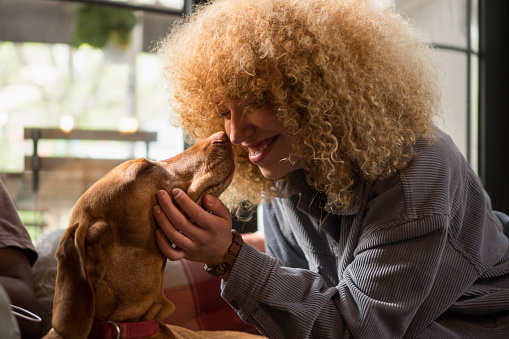 A beautiful young woman with curly hair is rubbing noses with her dog.