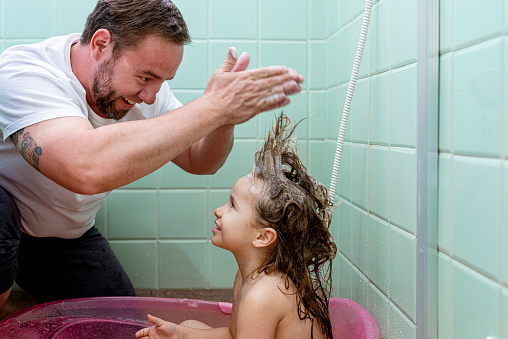Father playing with daughter's hair during bath.. Day in the life of father