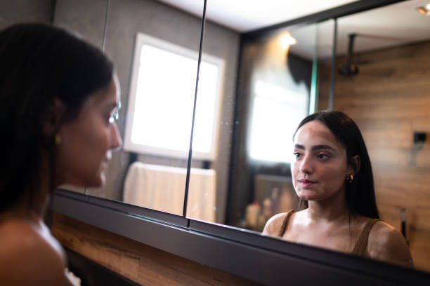 young woman with vitiligo looking in the mirror at home - mirror vanity women looking imagens e fotografias de stock