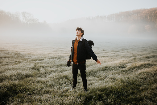 photographer taking pictures on a foggy meadow with open arms eyes closed