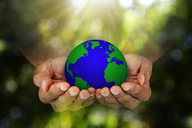 Hands holding planet earth on blurred green nature with sunlight background, environmental concept