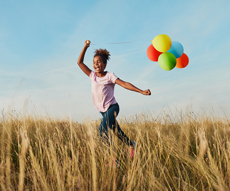 Happy little girl running playing with balloons outdoors