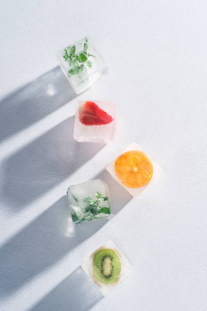 Frozen ice cubes with fruits, berries, herbs on a white background. Freezing is a safe method. Home food concept. Bright light, trending shadows. Top view with copy space