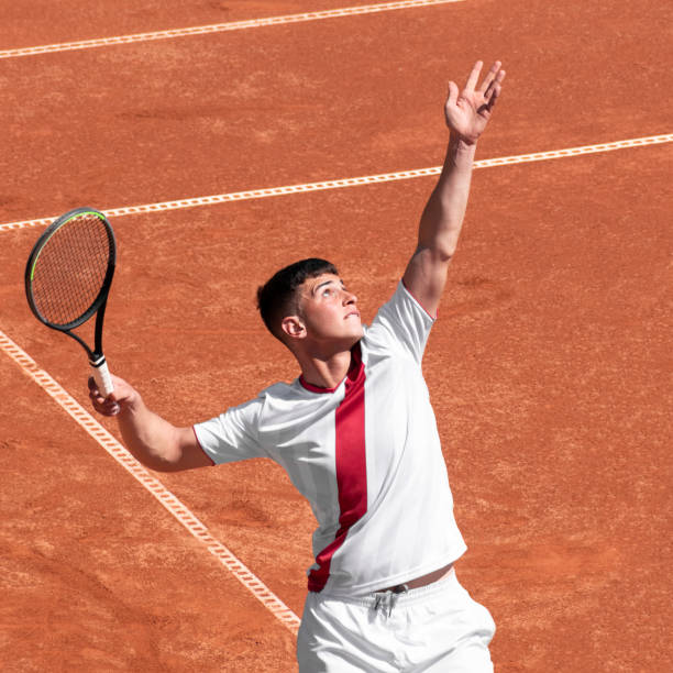 el joven tenista masculino realiza saques de pelota en pista de tenis de arcilla al inicio del partido. lindo atleta en acción. deporte individual y competitivo - tennis serving sport athlete fotografías e imágenes de stock