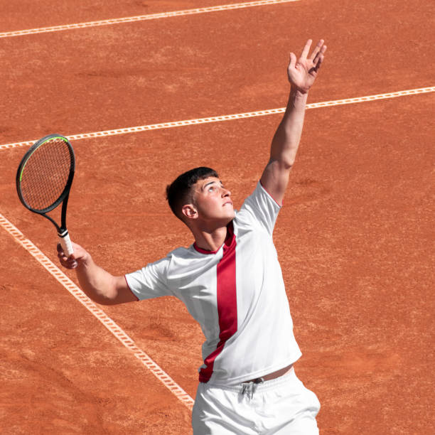Young male tennis player performs serves ball on clay tennis court at start of game. Cute man athlete in action. Individual, competitive sport Young male tennis player performs serves ball on clay tennis court at start of game. Cute man athlete in action. Individual, competitive sport tennis teenager sport playing stock pictures, royalty-free photos & images