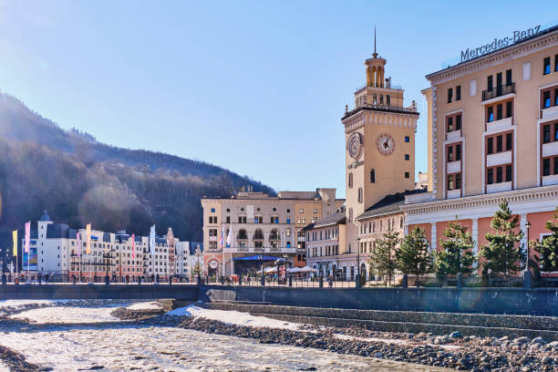 Ski resort Rosa Khutor. A view of the Mzymta River and town hall with clock on Rosa Square. Cityscape Sochi, Russia - March 4, 2020: Ski resort Rosa Khutor. A view of the Mzymta River and town hall with clock on Rosa Square. Cityscape sochi photos stock pictures, royalty-free photos & images