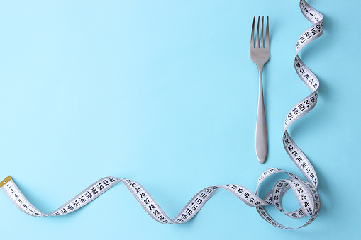 Measuring tape and fork on a colored background top view close-up. Weight loss, healthy eating, weight loss and control concept. High quality photo