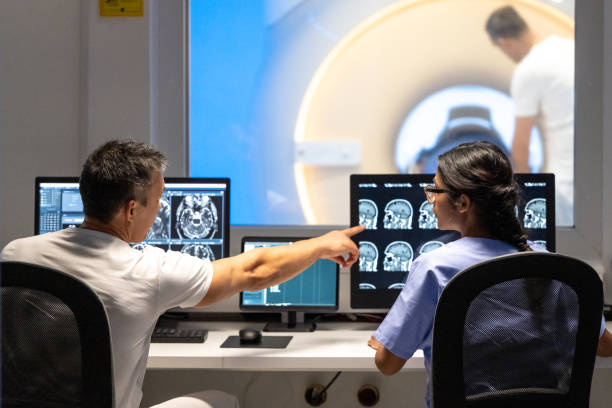 vista posteriore di due medici che analizzano i risultati della risonanza magnetica. uomo che punta le immagini sullo schermo del monitor. - radiologist computer doctor mri scan foto e immagini stock