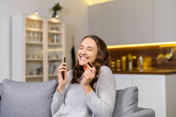 mujer feliz tiene teléfono inteligente y una tarjeta de crédito, compras en línea - greeting card holding women credit card fotografías e imágenes de stock