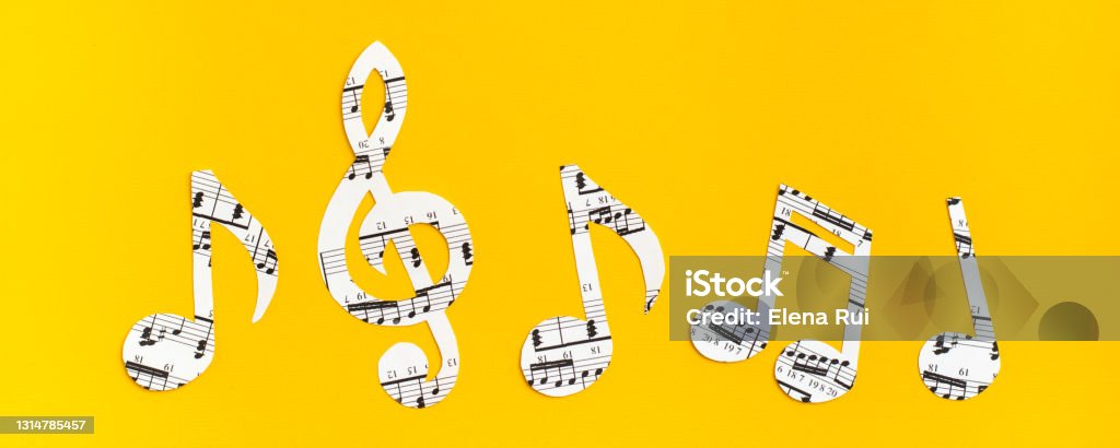 Musical notes and clef cut from paper with musical text in a row on yellow background. Web banner Music Stock Photo