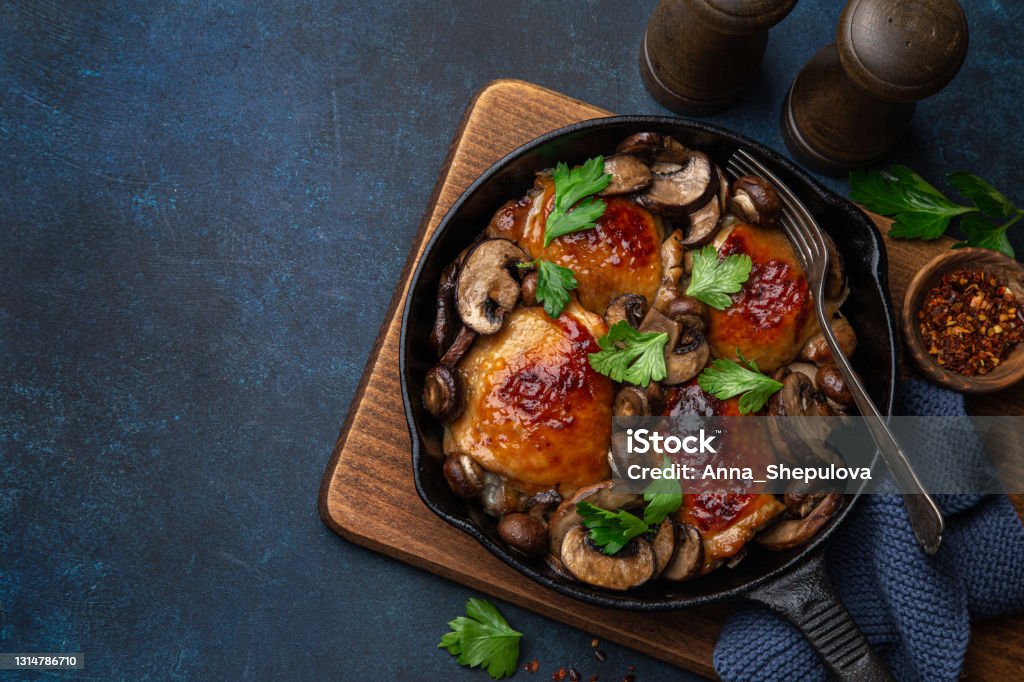 roasted  chicken thighs with mushrooms on cast iron  pan roasted  chicken thighs with mushrooms on cast iron  pan , dark blue concrete background, top view, copy space Chicken Thigh - Meat Stock Photo