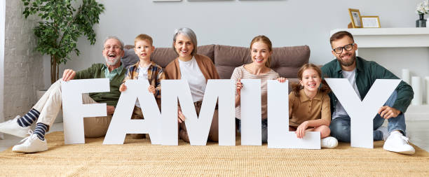 大家族は単語familyを保持し、座っている間にカメラを見て - grandmother senior adult smiling women ストックフォトと画像