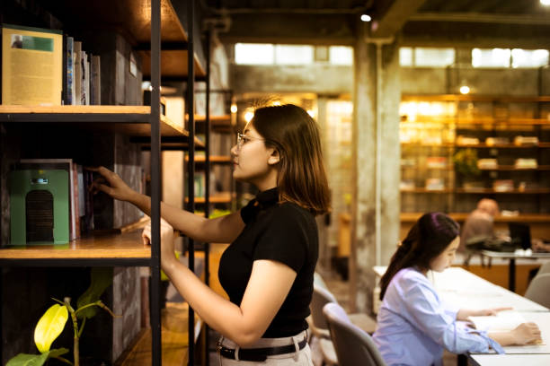 コミュニティカレッジの図書館の棚から本を選ぶ若い女子学生 - bookstore student chinese ethnicity book ストックフォトと画像