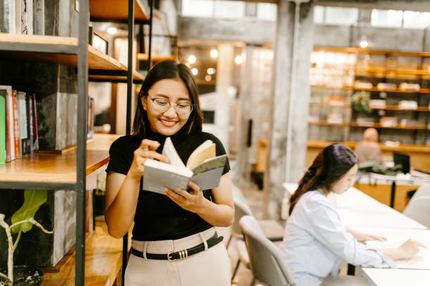 istock Young female student choosing book from shelf in library at community college 1314790099