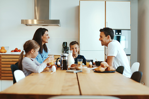 Smiling family talking together over a healthy breakfast around their kitchen table in the morning