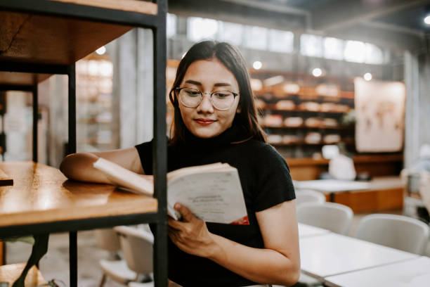 giovane studentessa che sceglie il libro dallo scaffale in biblioteca al community college - library education teenager student foto e immagini stock