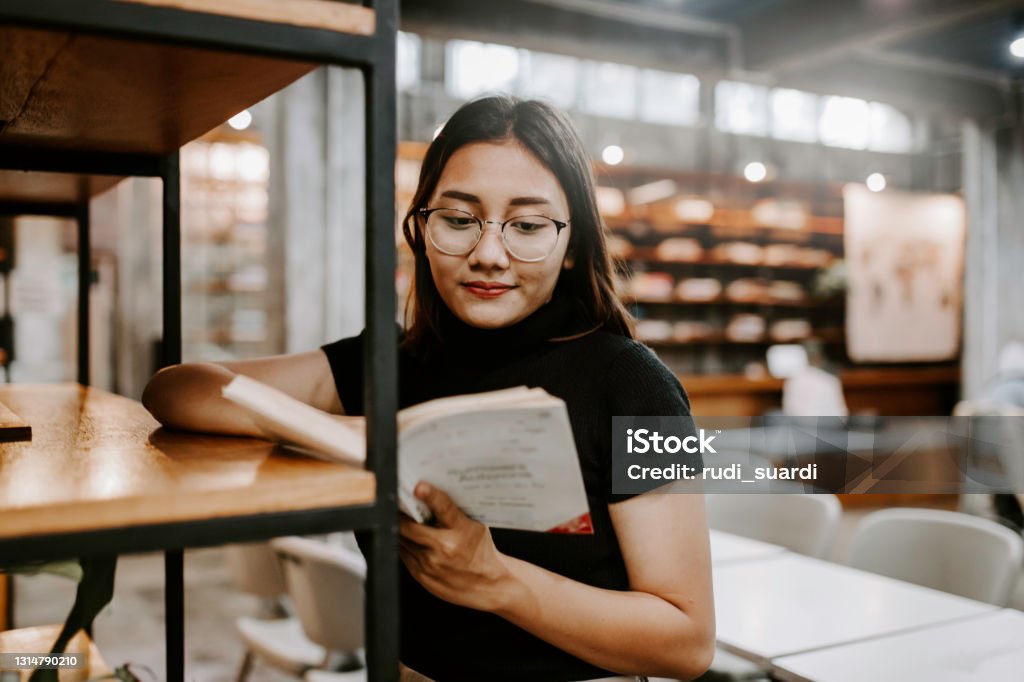 Young female student choosing book from shelf in library at community college asian woman choosing a book from bookshelf Book Stock Photo