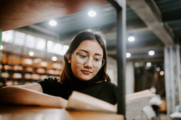 istock Young female student choosing book from shelf in library at community college 1314790216