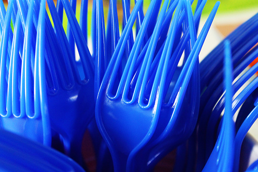 Close-up of a bunch of blue plastic forks stood up in a plastic cup, tines up.