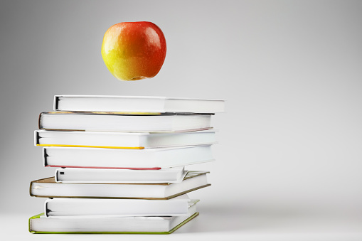A red Apple hovers over a stack of books on a light background. Concept of education and training.