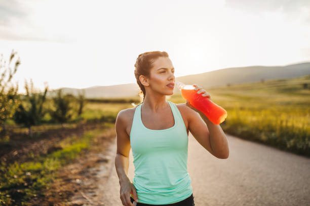 Attractive sportswoman is refreshing with cold drink after hard exercise Attractive young blonde sportswoman is refreshing with cold drink after jogging in nature on sunny summer day at sunset energy drink stock pictures, royalty-free photos & images
