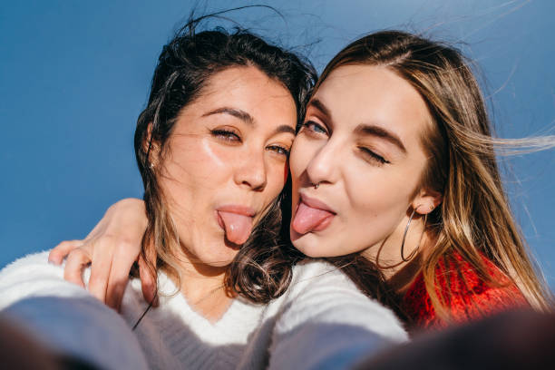 Couple of young girls sticking their tongues out while taking a selfie Close-up of a couple of young girls, one blonde and one brunette sticking out their tongues while taking a selfie. teenager couple child blond hair stock pictures, royalty-free photos & images