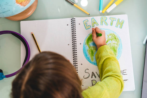 Top view of child girl draws planet earth with wax colors on school notebook for Earth day - Little activist girl writes the message Save the Planet - Protection of environment, global warming Top view of child girl draws planet earth with wax colors on school notebook for Earth day - Little activist girl writes the message Save the Planet - Protection of environment, global warming climate justice photos stock pictures, royalty-free photos & images