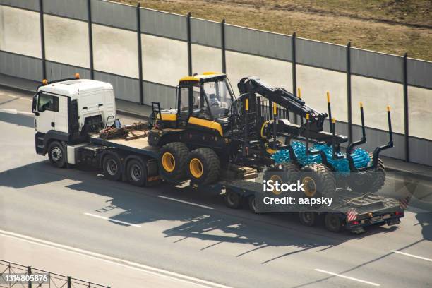 Transportation Of Equipment For Processing Forest Of Tree Trunks Forwarder Machines Wheeled Harvester Timber Industry On The Cargo Platform Of A Truck Trailer Stock Photo - Download Image Now