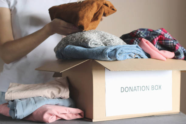 girl puts in a box with donations items. Volunteering girl puts in a box with donations items. Volunteering. High quality photo clothing donation stock pictures, royalty-free photos & images