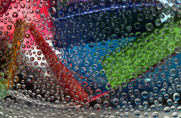 istock Translucent water droplets fall down against the pink-blue-gray background with multicolored geometric figures. Abstract fantasy. 3D render. 1314807011