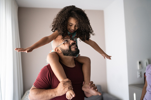 Padre cargando a su hija sobre hombros y jugando con ella en casa photo