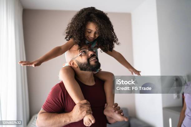 Father carrying daughter on shoulders and playing with her at home