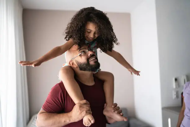 Photo of Father carrying daughter on shoulders and playing with her at home