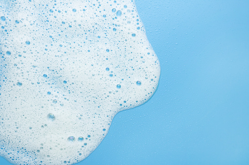 White foam, mousse on a blue background. Border for their foam text. The concept of foaming products, cosmetics or cleaning products.
