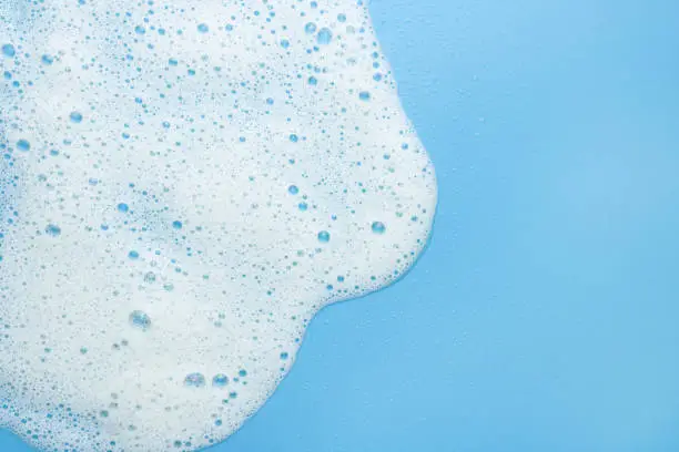 Photo of White foam, mousse on a blue background. Border for their foam text. The concept of foaming products, cosmetics or cleaning products.