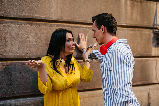 Young Caucasian couple arguing outdoors on street.