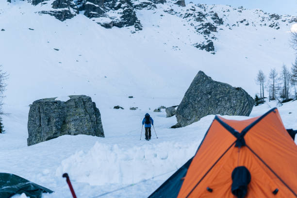 splitboarder leaves winter campsite and heads towards mountains - switzerland cold green rock imagens e fotografias de stock