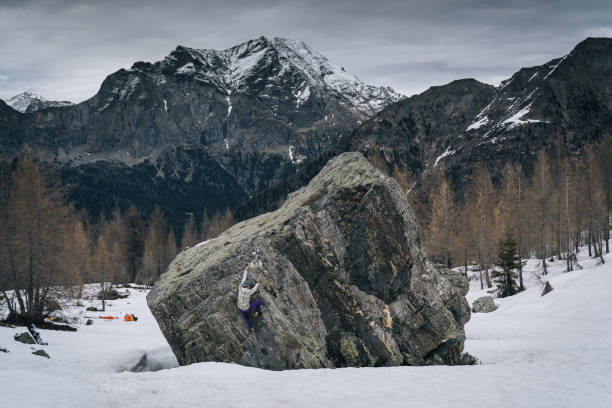 climber ascends steep boulder in snowy field - conquering adversity wilderness area aspirations achievement imagens e fotografias de stock