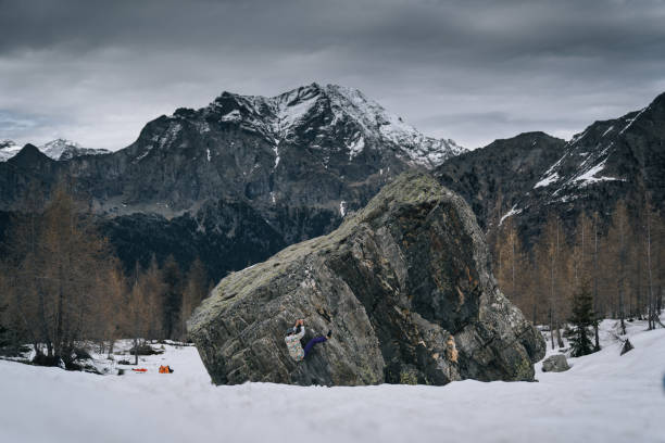 climber ascends steep boulder in snowy field - conquering adversity wilderness area aspirations achievement imagens e fotografias de stock