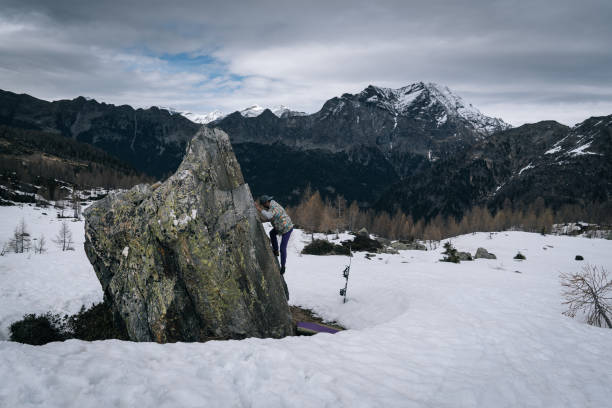 climber ascends steep boulder in snowy field - conquering adversity wilderness area aspirations achievement imagens e fotografias de stock