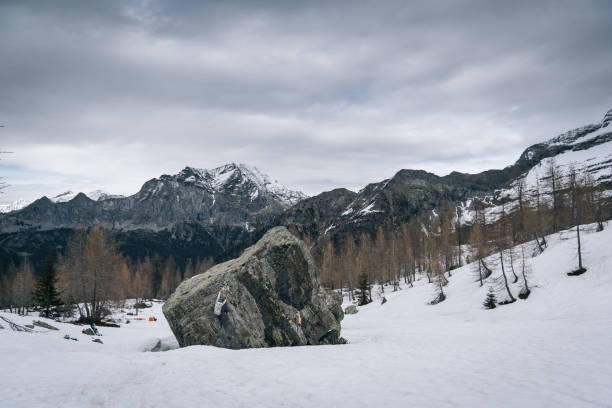 climber ascends steep boulder in snowy field - conquering adversity wilderness area aspirations achievement imagens e fotografias de stock