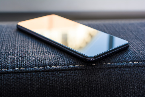 Business Smartphone With Reflection Lying On Armrest Of A Couch